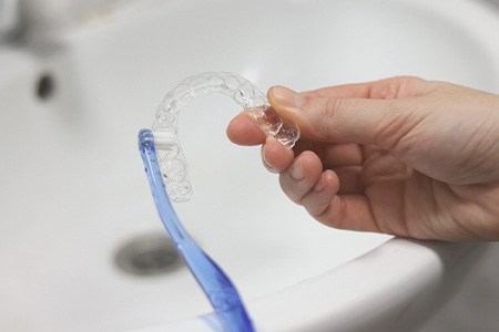 Patient cleaning clear aligner with toothbrush in sink