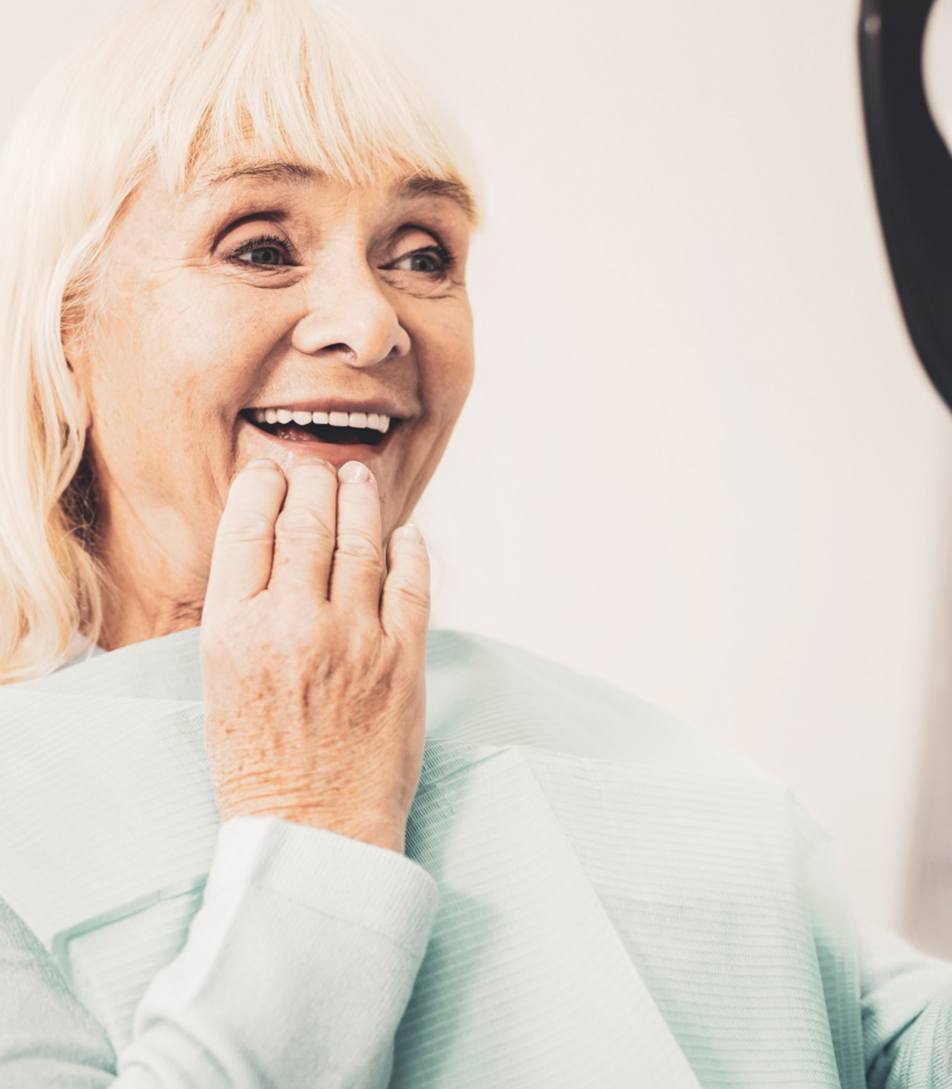 Senior woman using mirror to admire her new dentures