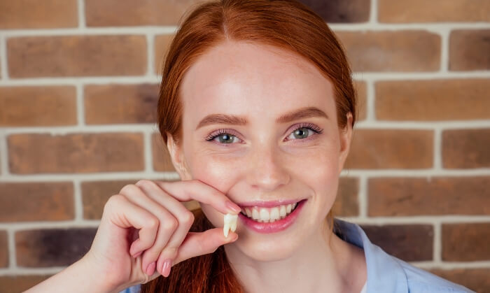 Woman smiling and holding an extracted tooth after restorative dentistry treatment
