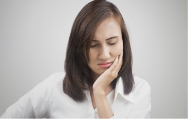 Woman holding cheek in pain before emergency dentistry